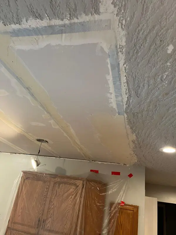 Cabinets wrapped in plastic with red tape while the popcorn ceiling is removed